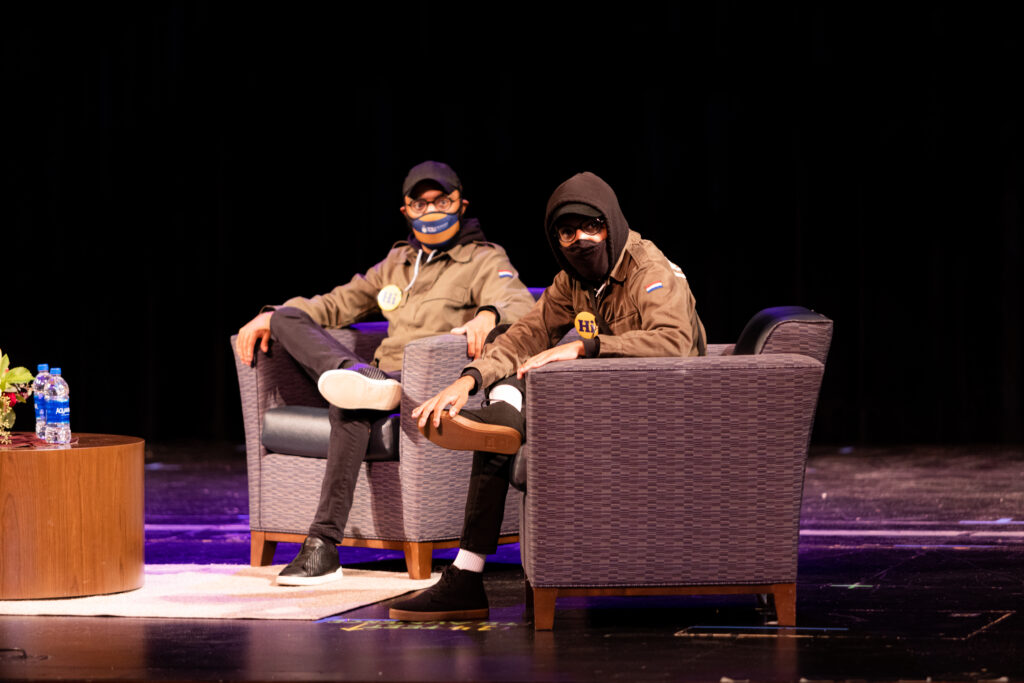 two masked men sitting in chairs on stage