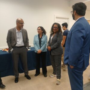 Dean of Humanities and Social Sciences Christopher Fisher, Dean of Business Sunita Ahlawat, Assemblywoman Verlina Reynolds-Jackson, and one additional male facing away from the camera standing and interacting with one another in a common area near a table to snacks.